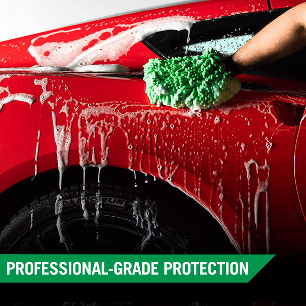 A hand uses a wash mitt covered in thick foam to scrub the surface of a red car. 