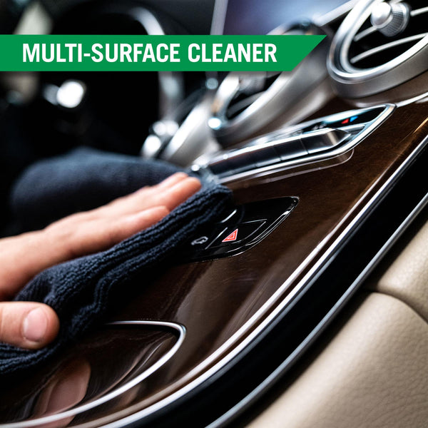 A hand uses a microfiber towel to clean the dashboard of a car, highlighting the multi-surface cleaning capabilities of the kit. 